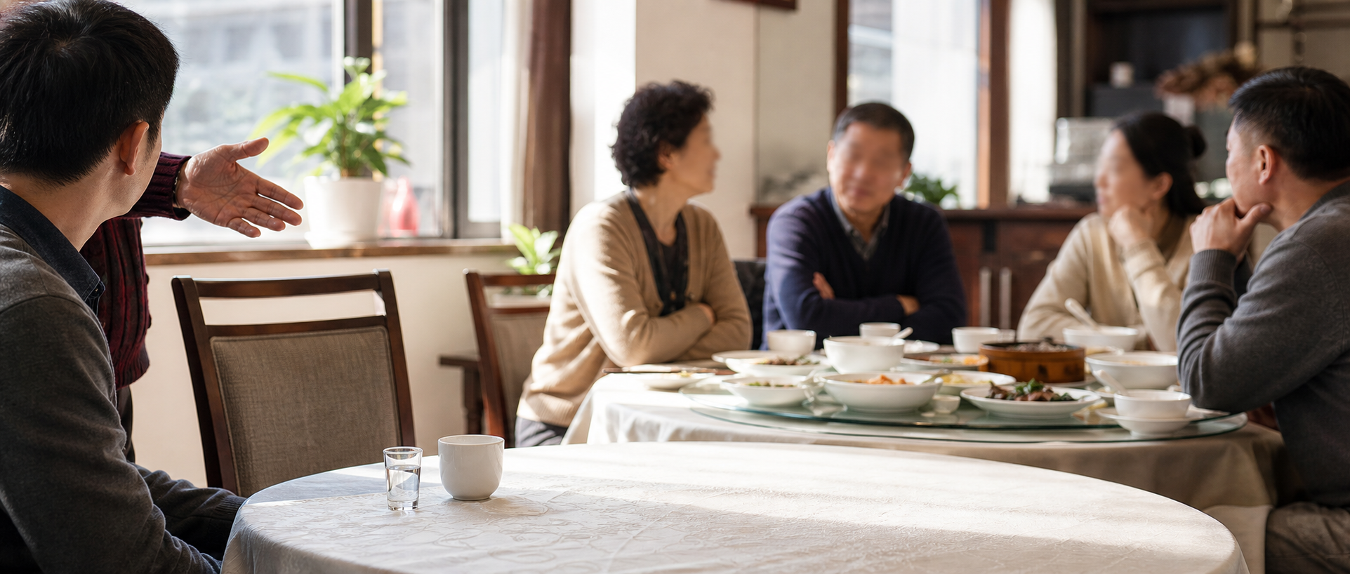 An anonymous drinker at a restaurant table facing an empty chair and an unexpected family conversation